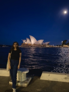 Nadia stands in front of the Sydney opera house at night with a dark blue sky