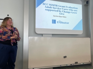 Kirsty Rose Parker, Director of The Evaluator stands next to a white board at the University of Birmingham, to present our findings on Service User voice. 